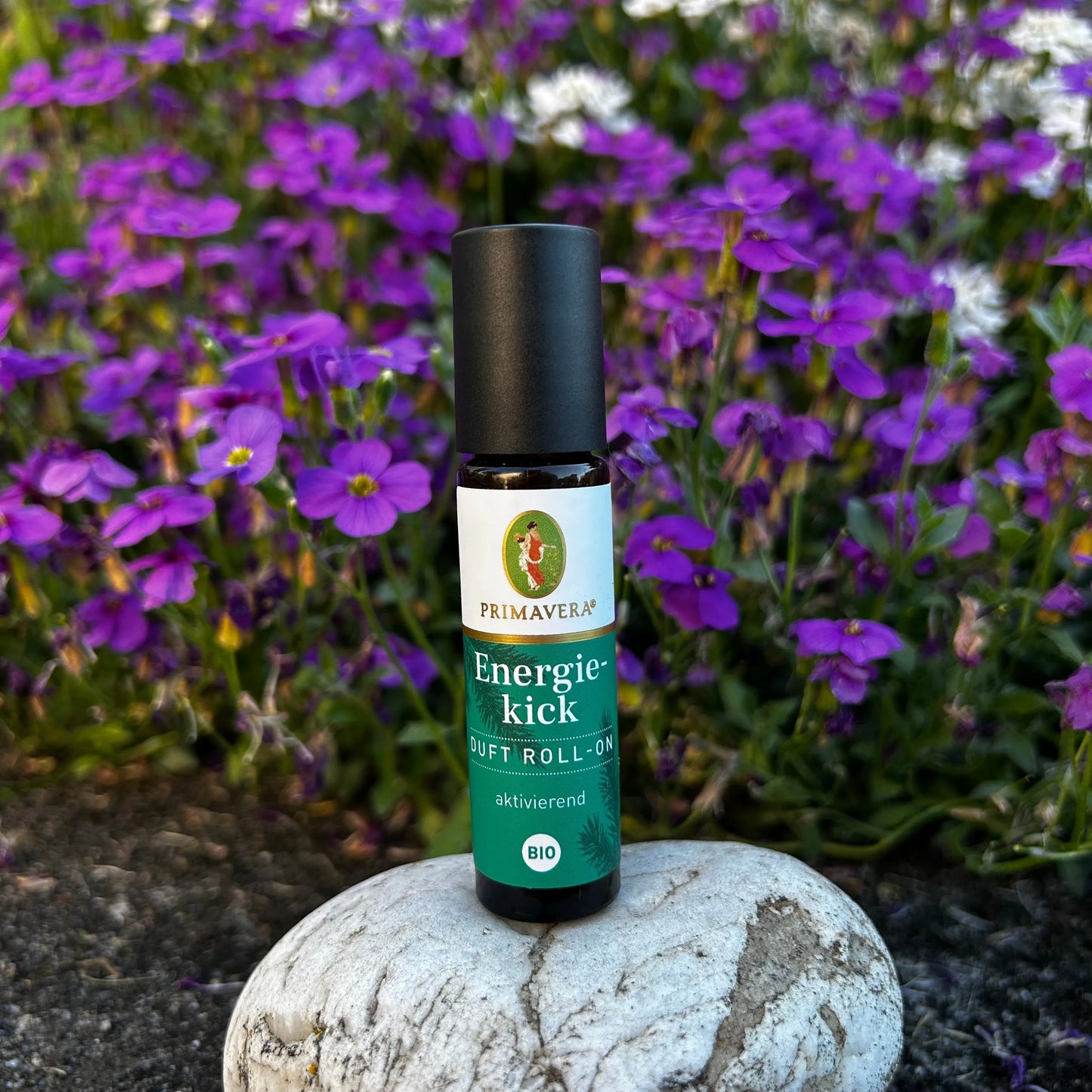 Energiekick Duft-Roll-On steht auf einem Stein vor einer violett weissen Blumenwiese.