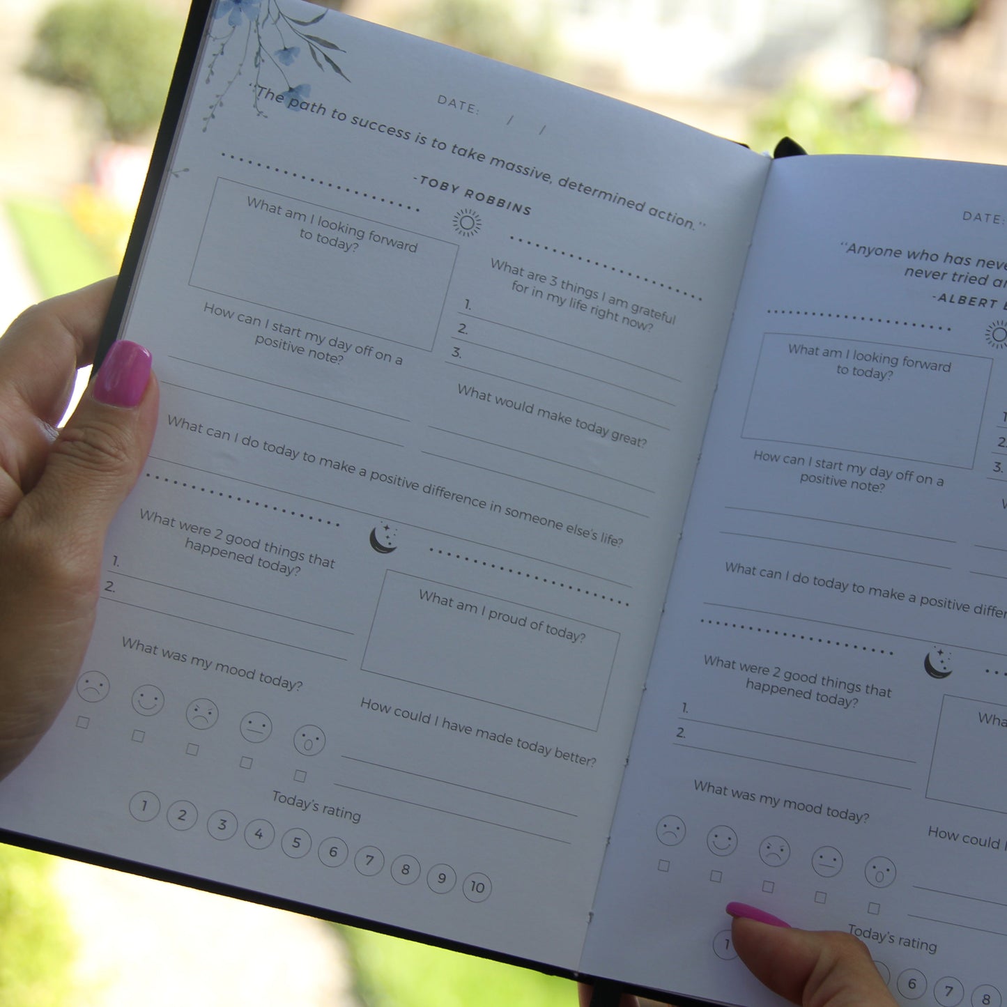 Frau hält geöffnetes Journal mit Reflexionsfragen in der Hand, pink lackierte Nägel sichtbar.