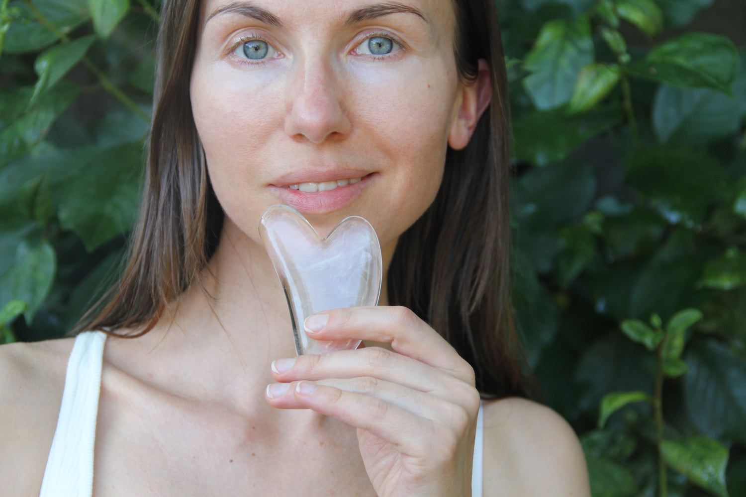 Gua Sha in der Hand vor dem Gesicht einer lächelnden Dame