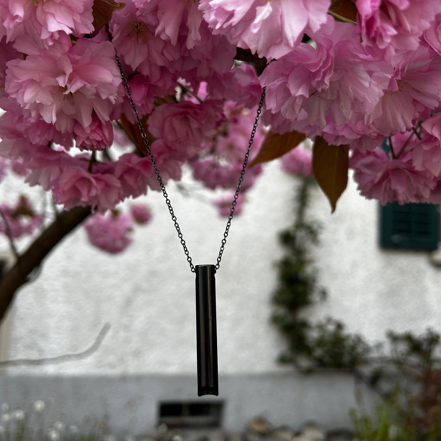 Schwarze Halskette zur Tiefenatmung hängt an einem blühenden Kirschbaumast