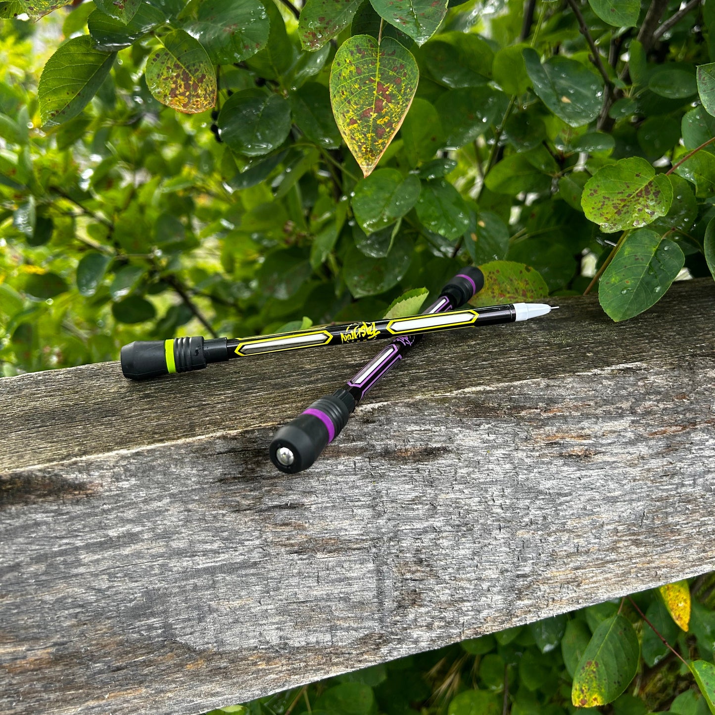 2 Kugelschreiber auf einem Holzgeländer vor grünem Strauch