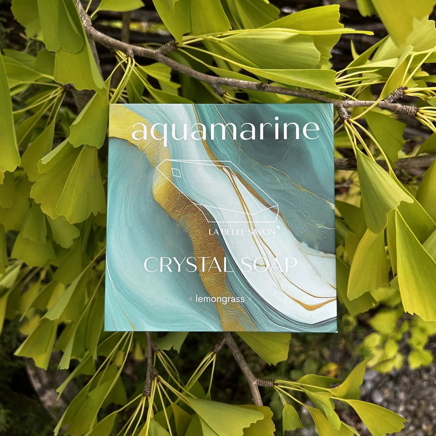 Die aquamarine Crystal Soap liegt verpackt auf Ästen mit grünen Blättern.