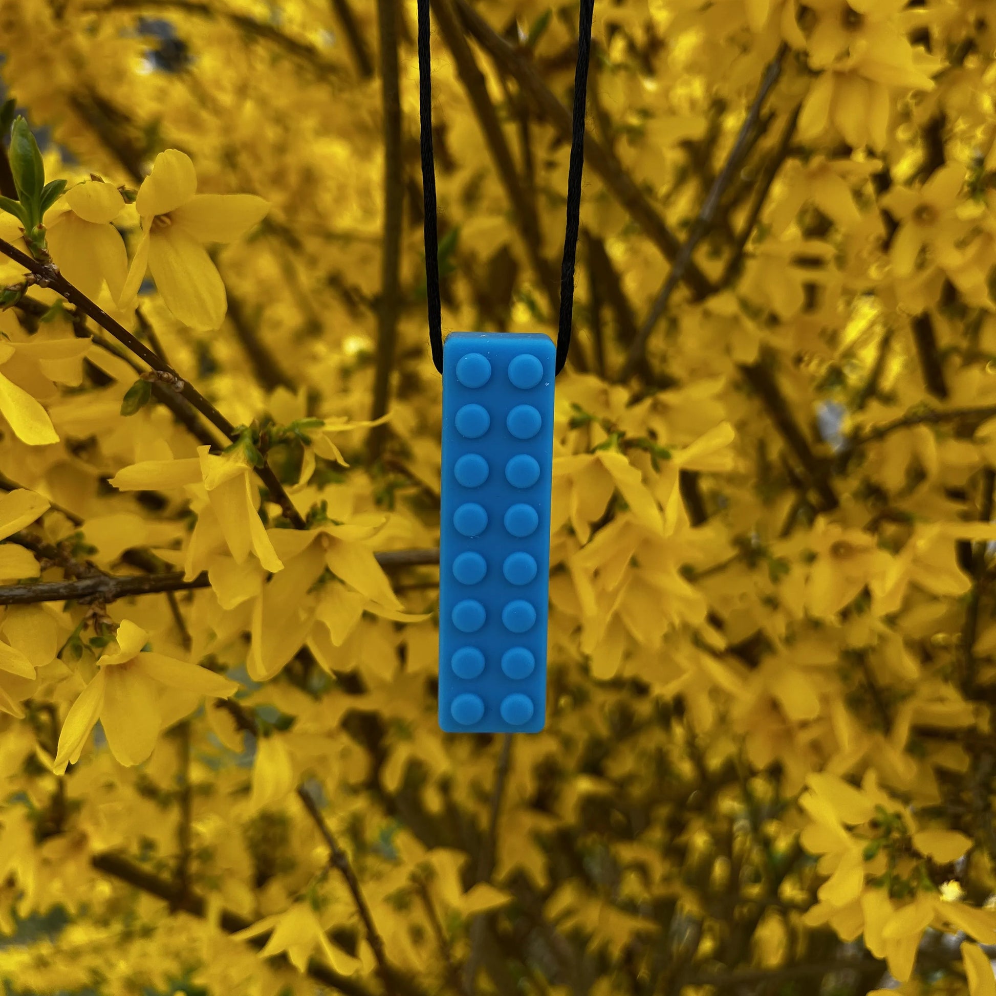 Beisserchen Kette in blau hängt am Ast eines Baumes mit gelben Blüten