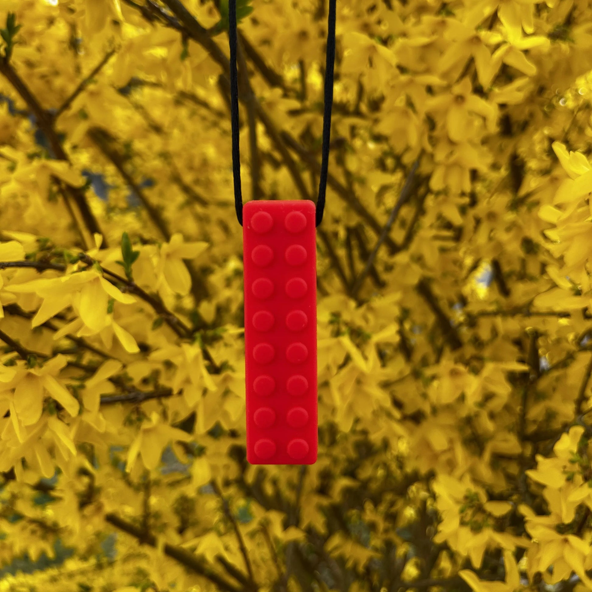 Beisserchen Kette in rot hängt am Ast eines Baumes mit gelben Blüten