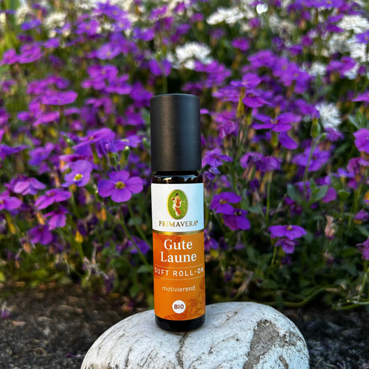Motivierender Duft-Roll-On steht auf einem Stein vor einer violett-weissen Blumenwiese.