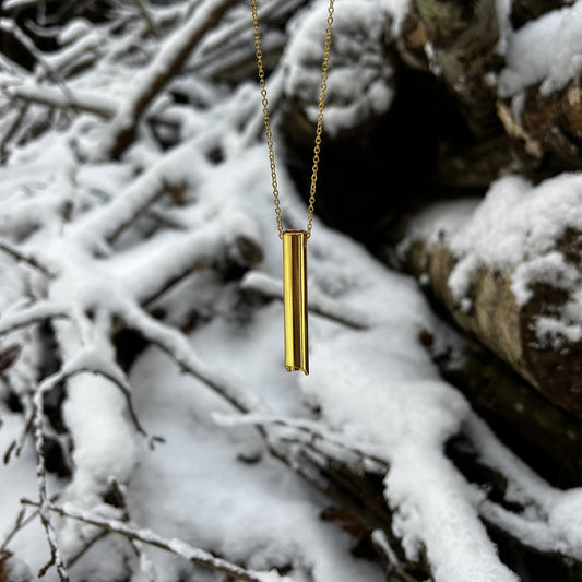 Goldene Halskette zur Tiefenatmung hängt vor einem Schnee bedeckten Holzhaufen.