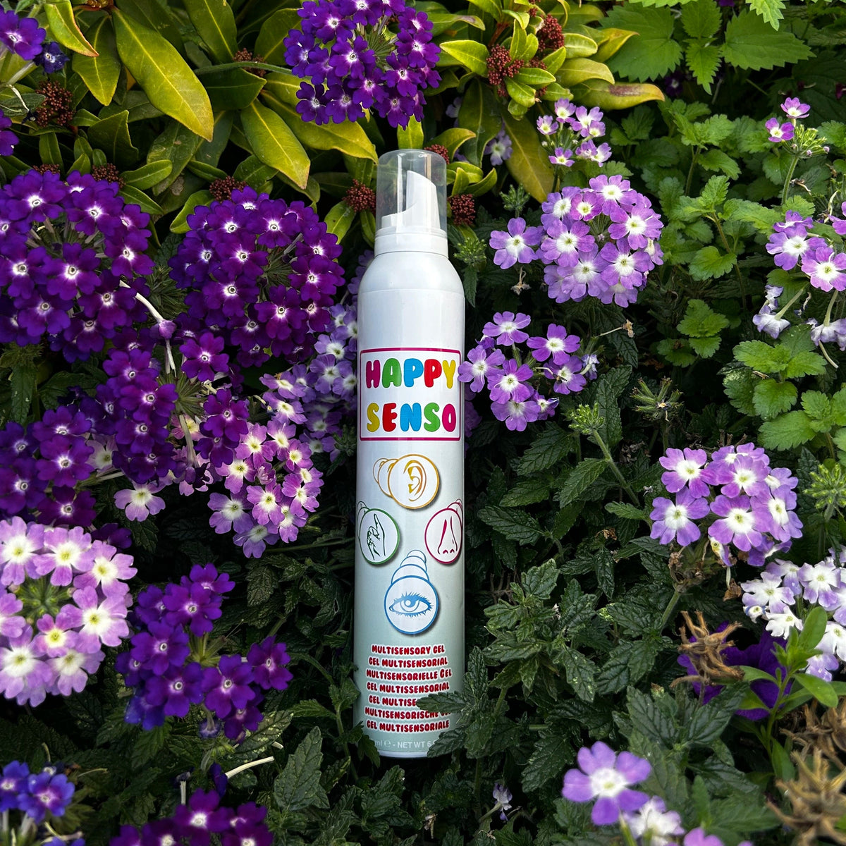 Happy Senso Schaum Spray (grün) liegt auf einem Busch mit violetten Blumen