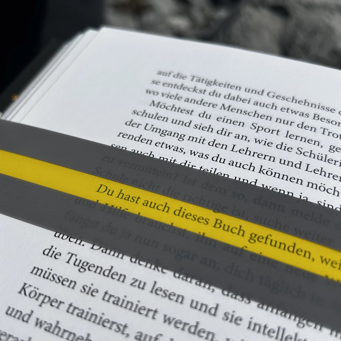 Ein Buch ist aufgeschlagen. Der Text er ersten Seite ist fokussiert. Ein gelber Streifen liegt auf dem Buch. Es markiert eine Zeile. 